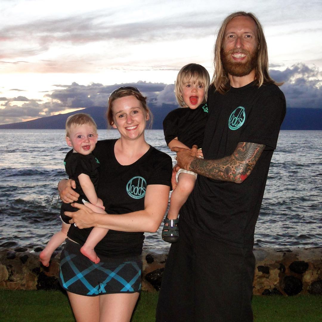 Todd Huhman with his wife and two children on a Pacific Northwest shoreline at sunset, all in black Todd's-branded shirts.
